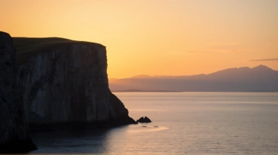 Rugged Cliffside Beside Shimmering Water At Dusk