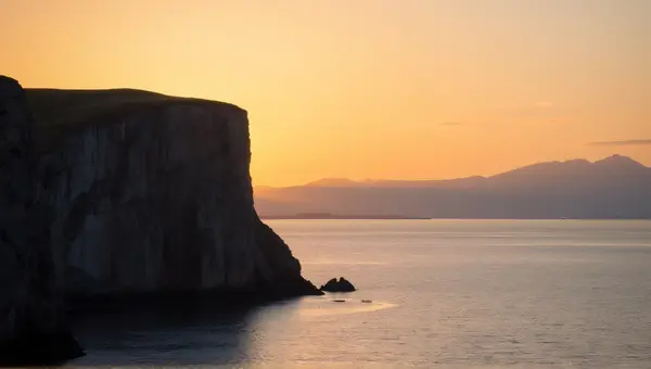 Rugged Cliffside Beside Shimmering Water At Dusk