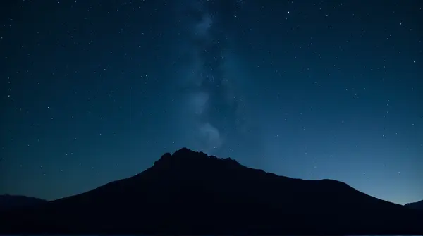 Low angle view of a rugged mountain ridge beneath a sky filled with countless twinkling stars.