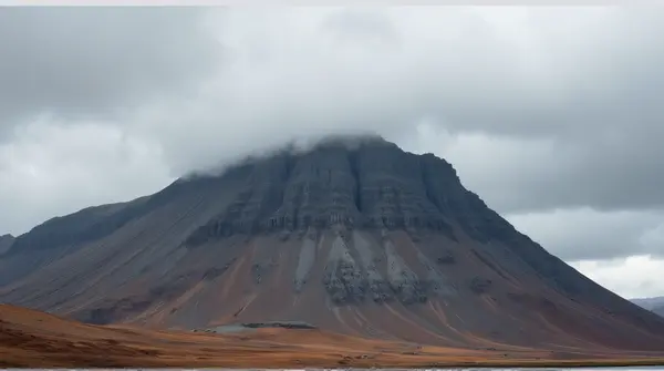 Low angle view of a rugged brown and grey mountain with thick layered gray clouds overhead.