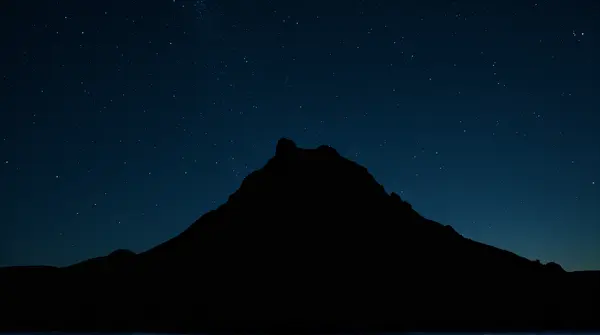 Silhouette of a rugged peak outlined against a dark sky filled with twinkling lights.
