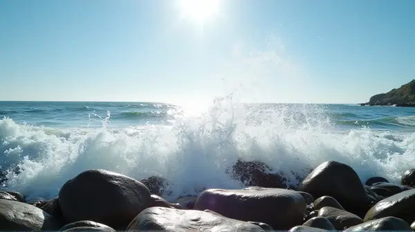Waves striking rugged seaside stones under bright sunlight with clear sky background.