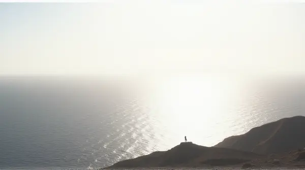 Wide shimmering surface extending toward horizon bordered by rugged terrain under pale sky
