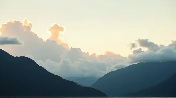 Dark silhouetted peaks stretch across the horizon beneath soft sunlight and pale vapor clouds.
