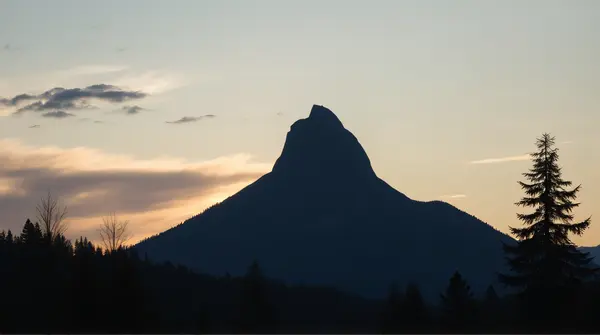 Dark silhouette of a tall peak outlined against a fading sky with sparse trees and wispy clouds.