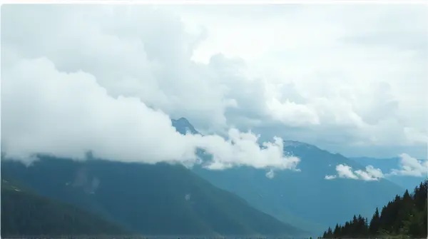 Low view of green and slate-colored peaks under a bright sky with soft white clouds