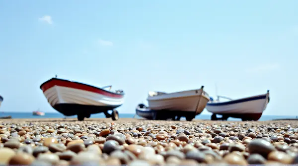 Small boats moored on a pebbled coastline with detailed hulls under a clear blue sky