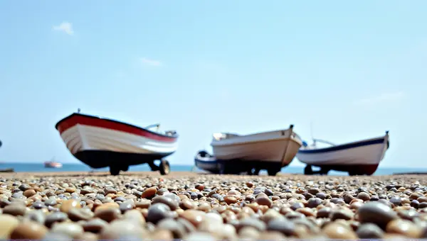 Small Boats Moored On Pebbled Coastline Under Clear Sky