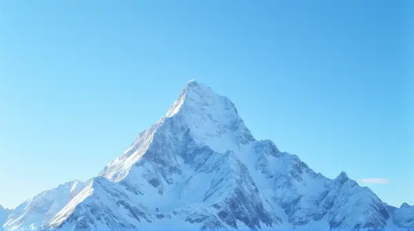 Low angle view of a towering mountain with snow-covered rugged slopes and sharp ridges under a clear blue sky.