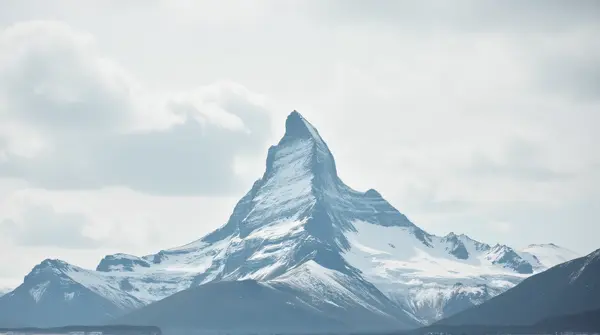 Low-angle view of a snow-covered mountain peak against a soft overcast sky in bright daylight.