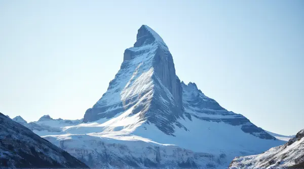 Low-angle view of a tall mountain covered in snow beneath a clear blue sky