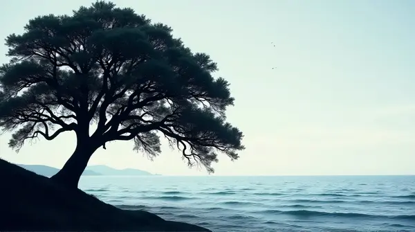 Dark outline of a large oak tree next to a vast water body with gentle waves under a clear sky.