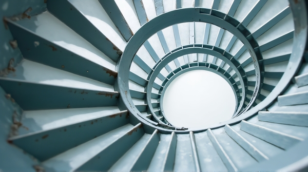 Close-up view of a steel helix staircase showing circular pattern from below against a neutral background.
