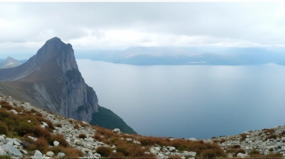 Towering Peak Beside Expansive Water Under Cloudy Sky