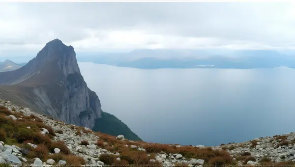 Towering Peak Beside Expansive Water Under Cloudy Sky