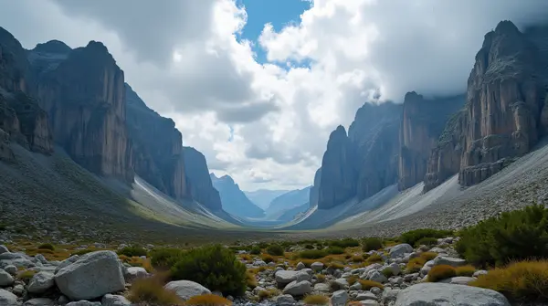 Wide-angle view of tall rocky peaks beneath a dynamic sky with rugged terrain and sparse plants in foreground