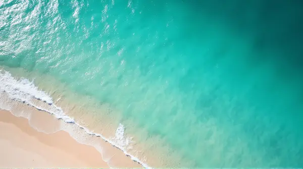 Top-down view of turquoise ocean blending into pale beach with sunlight reflections on water