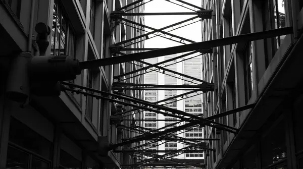 Grayscale image showing a complex metal framework with intersecting lines and contrasting light and shadow in a city environment