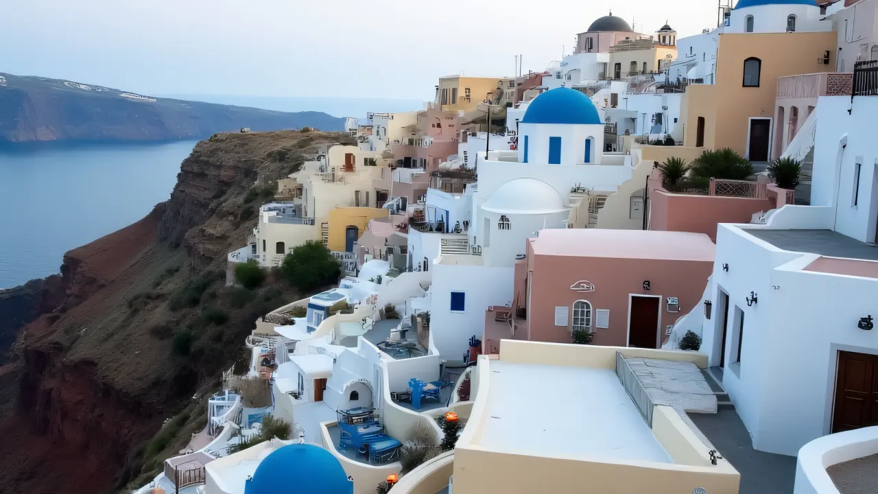 Aerial view of white and blue buildings on a coastal cliff with winding alleys under an overcast sky.