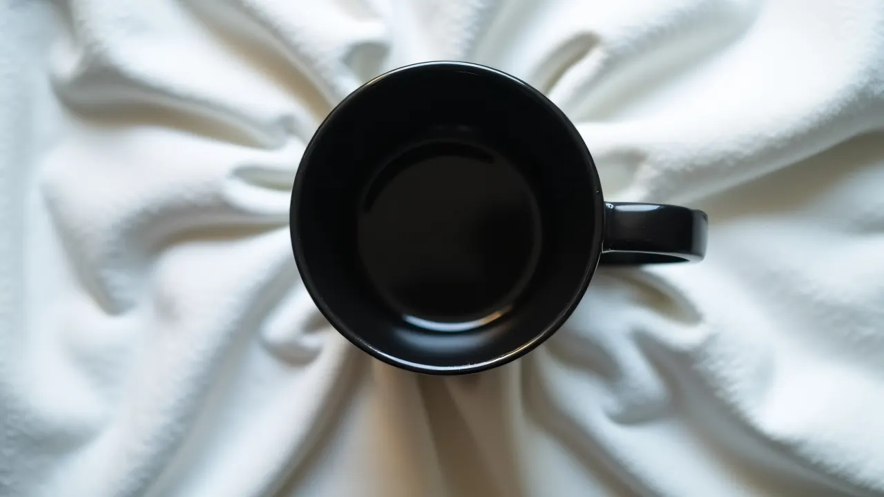 A black ceramic mug placed on wrinkled white linen fabric, showcasing its texture in soft lighting.