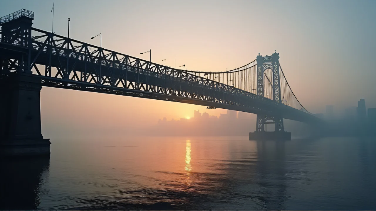 Low-angle view of a black metal bridge over a foggy river at dawn.