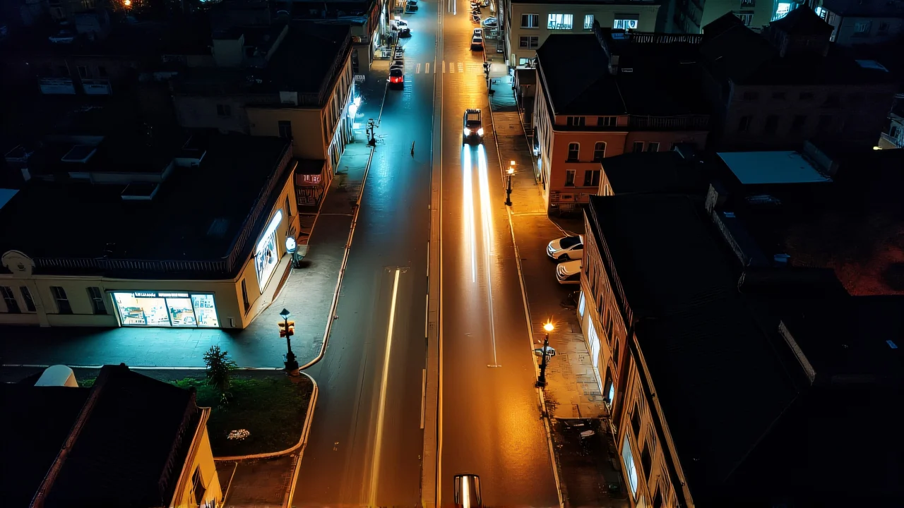 Aerial view of a city street at night with light trails and reflections on wet pavement.
