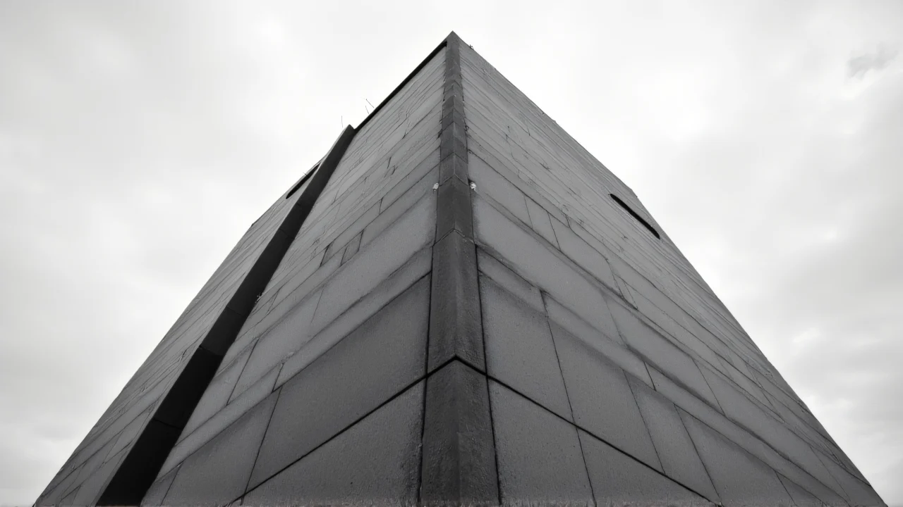 Grayscale image showcasing a concrete tower block from a low angle with textured facade and cloudy sky.
