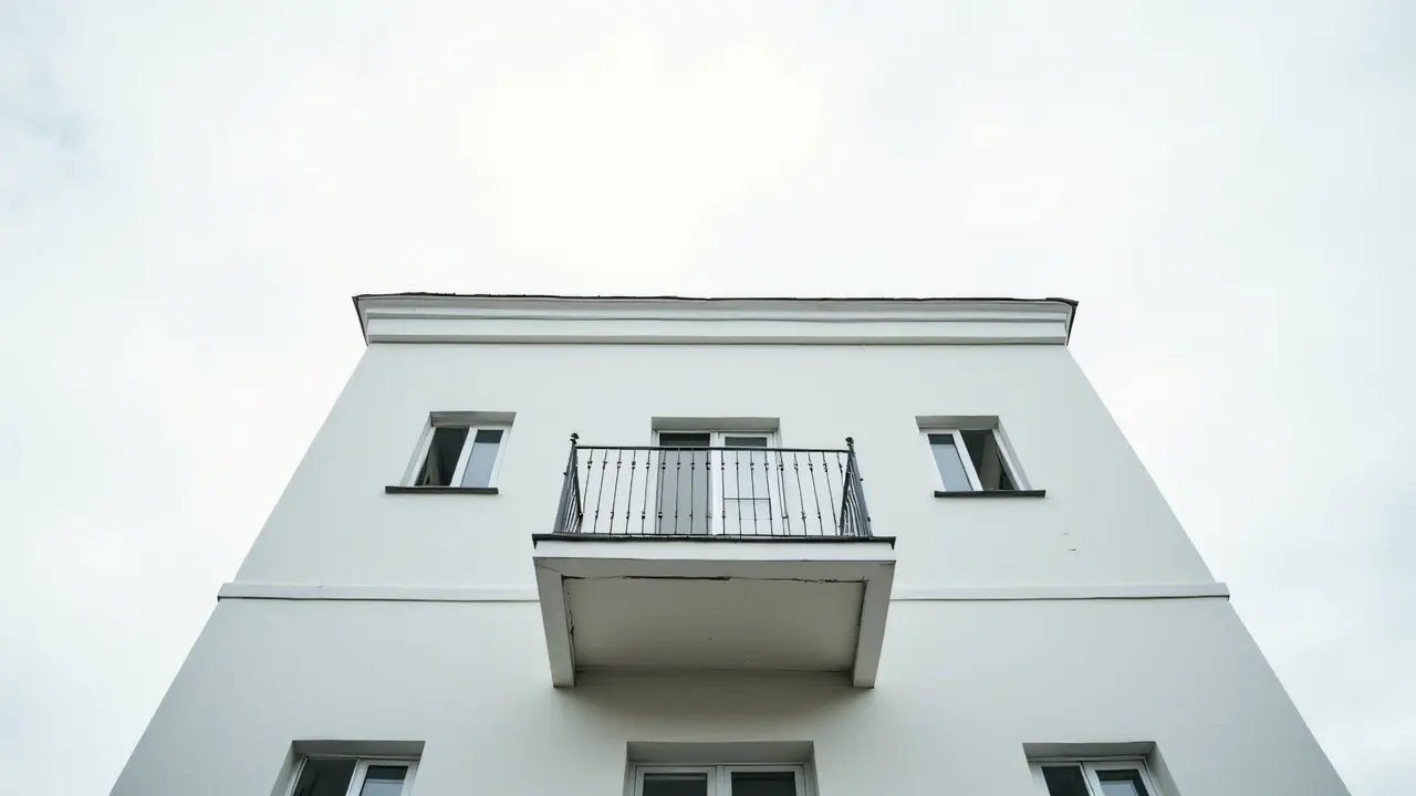 A low-angle view of a modern white concrete building featuring a balcony under a muted sky.