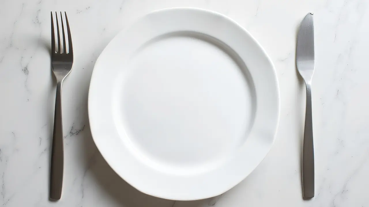 Overhead view of a porcelain plate and stainless forks in soft light.