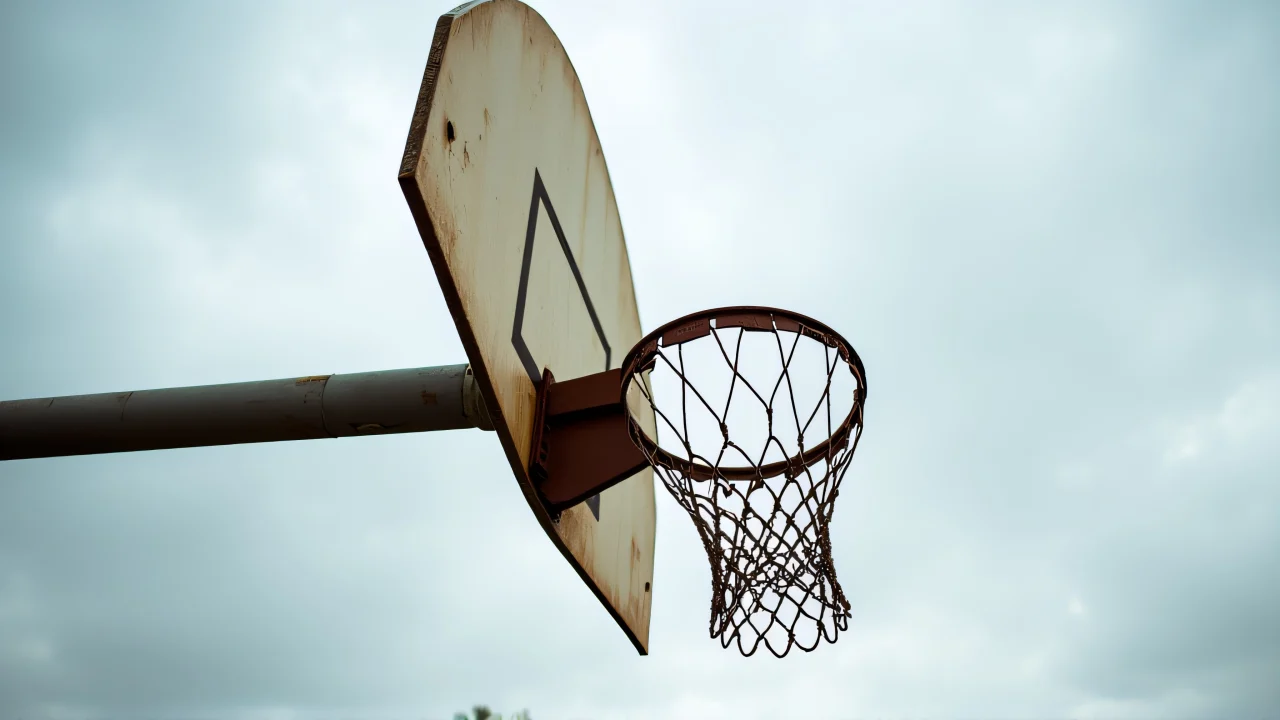 Low-angle view of a rusted basketball hoop against a cloudy sky.