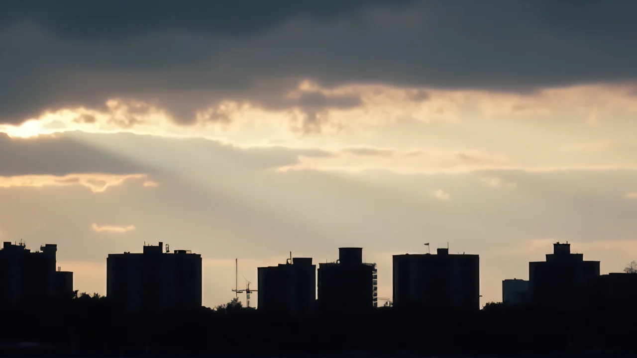 Silhouetted buildings against a colorful evening sky with layered clouds and strong backlighting.