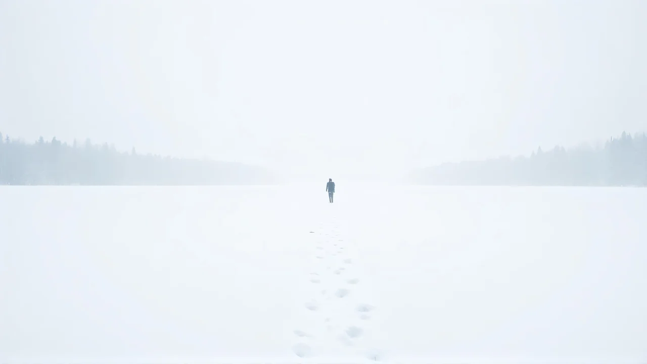 A wide snowfield with footprints leading to distant trees under a pale sky.