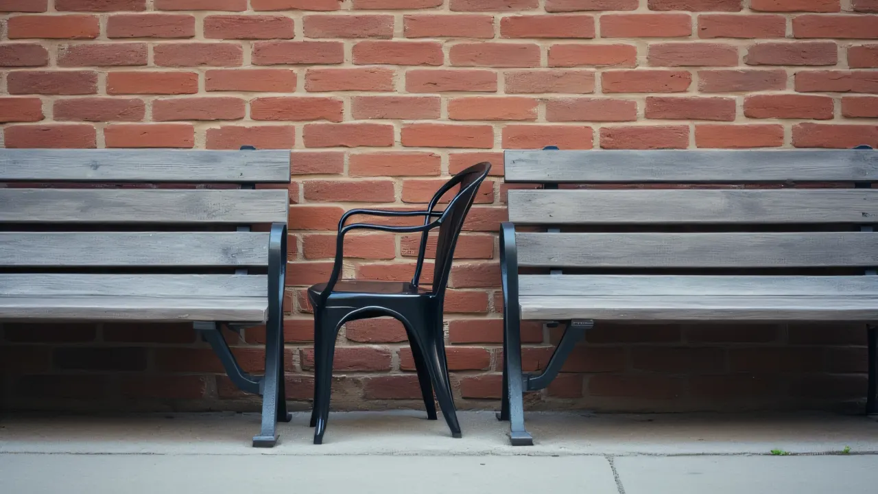 Two gray benches and a black chair by a textured brick wall.