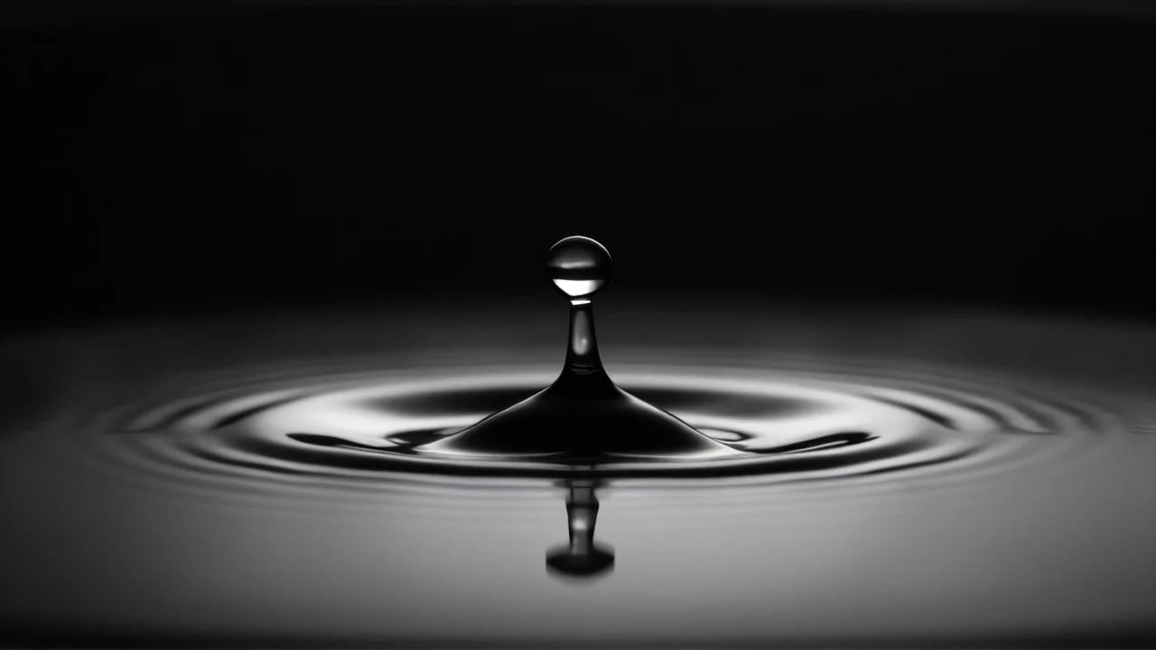 Close-up of a single water drop above a reflective surface.