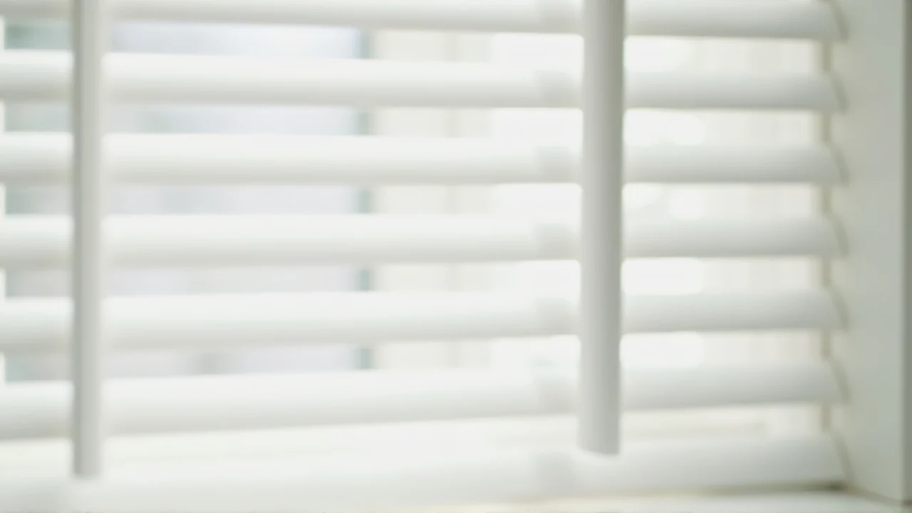 Close-up of white wooden window blinds casting soft shadows in morning light.